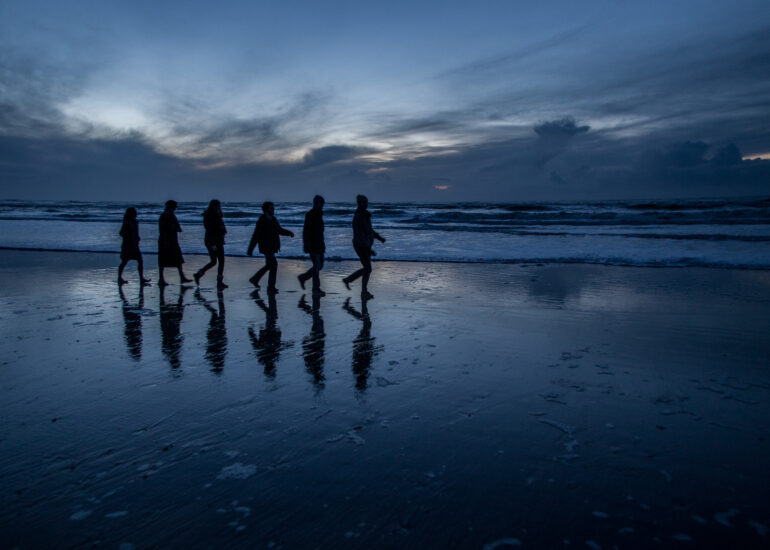 Pascal Meyer - Silhouettes de six personnes en file indienne sur une plage à la nuit tombante