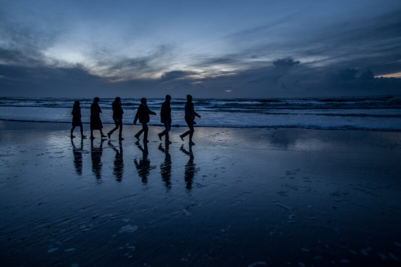 Pascal Meyer - Silhouettes de six personnes en file indienne sur une plage à la nuit tombante