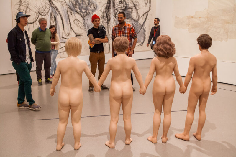 Pascal Meyer - Un groupe de touristes fait face, dans un musée, à quatre statues réalistes représentant des personnes nues